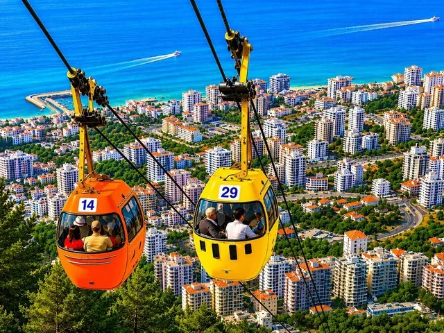 Cable cars travelling over a coastal city with the ocean in the background.