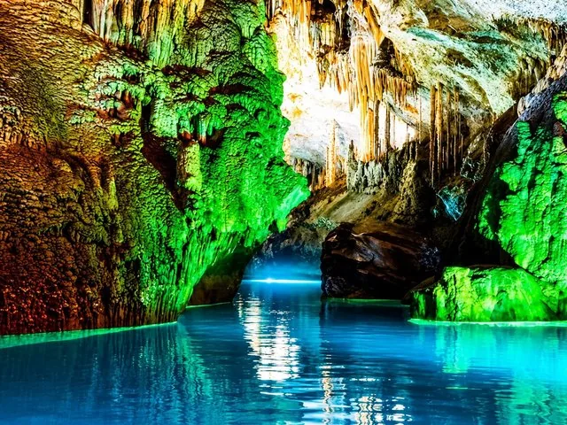 Stunning illuminated cave interior with stalactites and blue water pool