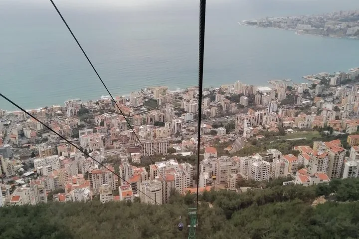 Blick aus einer Seilbahn hinab auf eine Stadt, die sich bis zum Meer erstreckt.