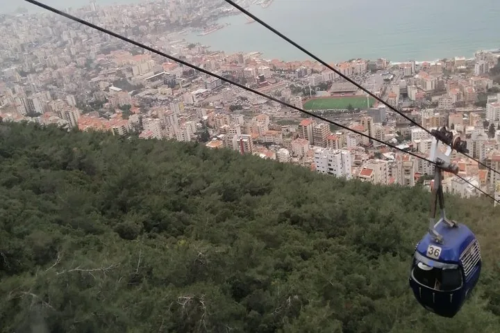 Un téléphérique bleu suspendu au-dessus d’une colline boisée, avec une ville en arrière-plan.
