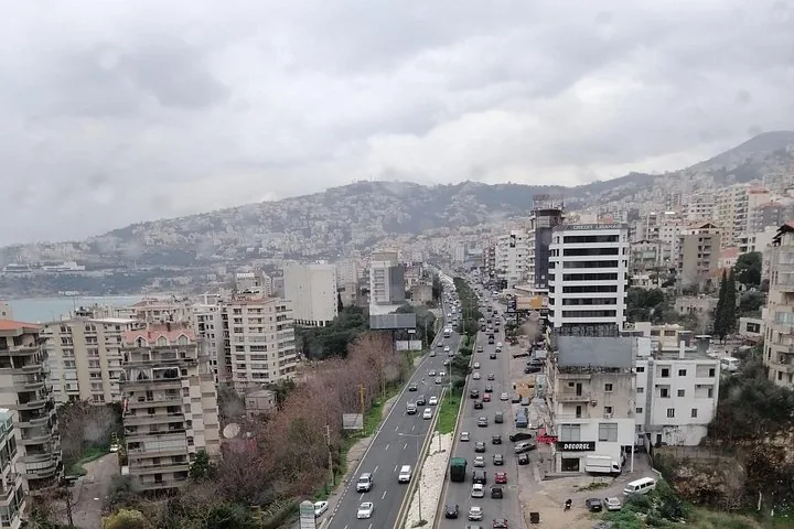 Elevated view of a busy highway cutting through a city with rolling hills behind.