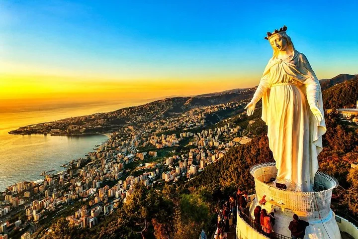 Large statue of Virgin Mary overlooking coastal city at sunset