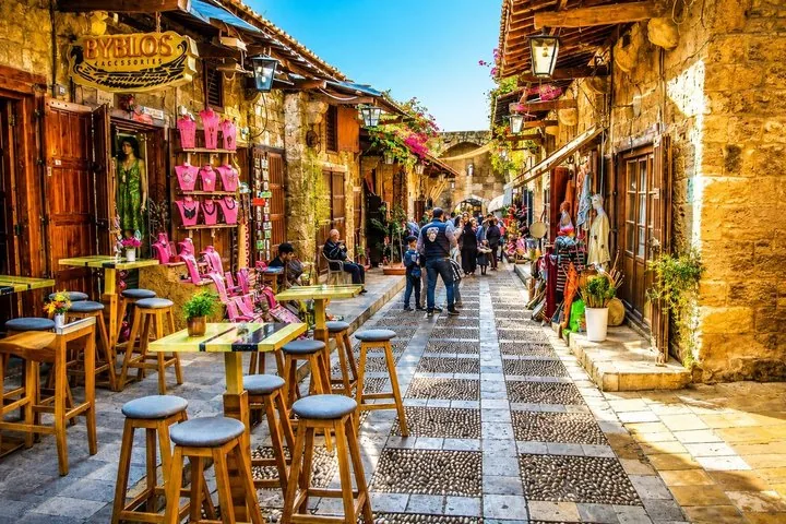 Kopfsteinpflasterstraße in Byblos mit Geschäften, Außensitzplätzen und Fußgängern.